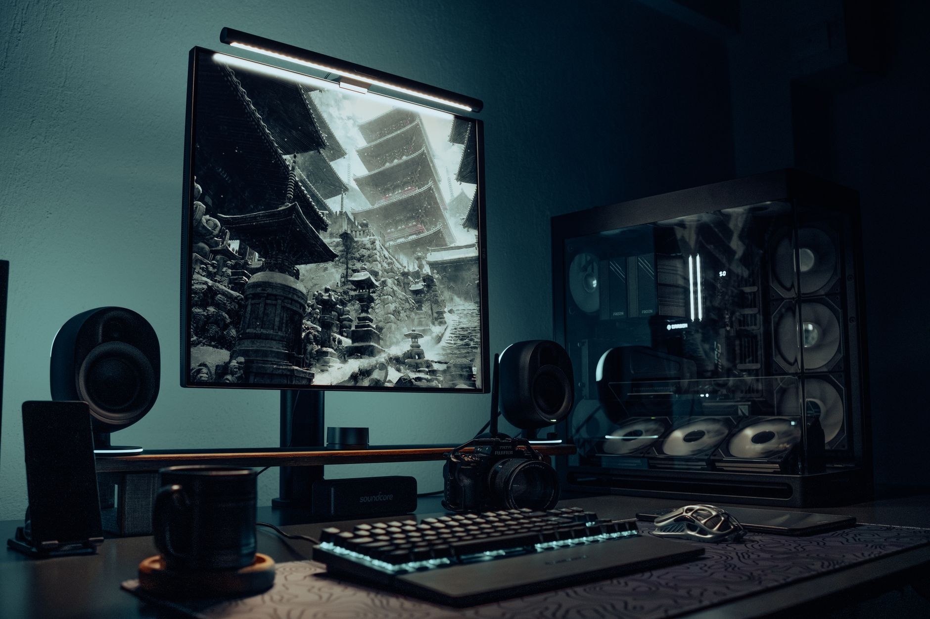 Bureau sombre avec un PC à boîtier vitré, un écran affichant une pagode, un clavier mécanique lumineux, une souris, des enceintes et une tasse.