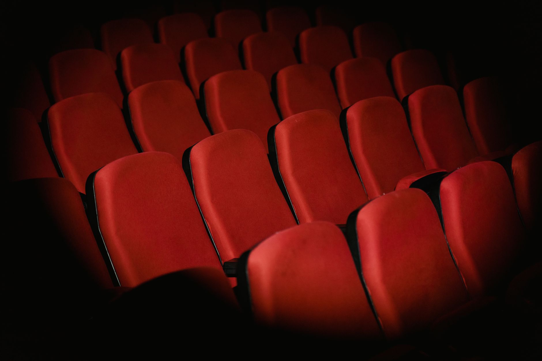 Rangées de fauteuils rouges vides dans une salle de cinéma plongée dans la pénombre.
