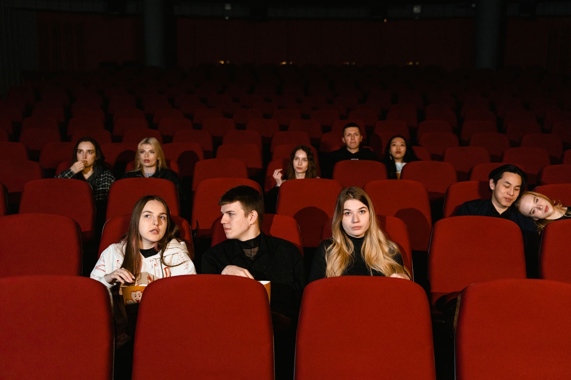 Spectateurs assis dans une salle de cinéma sombre aux fauteuils rouges, dont une personne qui mange du pop-corn.